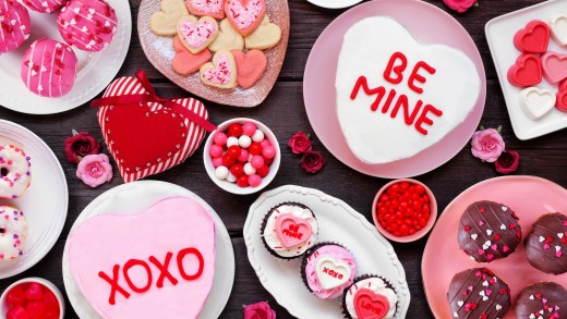 Valentines Day table scene with a selection of fun desserts and sweets. Above view on a dark wood background. Love and hearts theme.